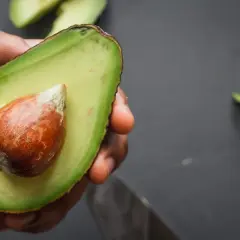 Mano che tiene mezzo avocado maturo con nocciolo. Ecco come si mangia l'avocado: fresco, cremoso, delizioso.