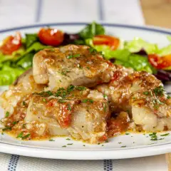 Deliziosa coda di rospo in umido con pomodoro e prezzemolo, servita con insalata fresca e spicchi di limone.