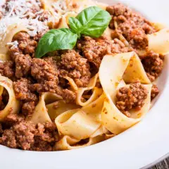 Pappardelle al ragù, un classico dei cibi tipici Emilia Romagna, con basilico fresco e parmigiano.