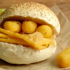 Pane e panelle, un panino ripieno di croccanti panelle e arancini, con fette d'arancia e lime sullo sfondo.