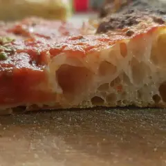 Fetta di pizza con pomodoro e un impasto pizza lievitazione 8 ore, soffice e alveolato, con crosta dorata.