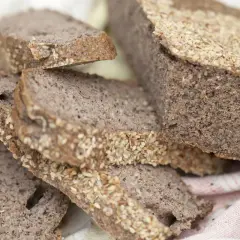Fette di pane di grano saraceno con semi di sesamo, su un panno bianco e rosa.