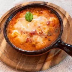 Piatto fumante di gnocchi al forno, uno dei piatti tipici della Campania, con pomodoro e mozzarella filante, guarnito con basilico.