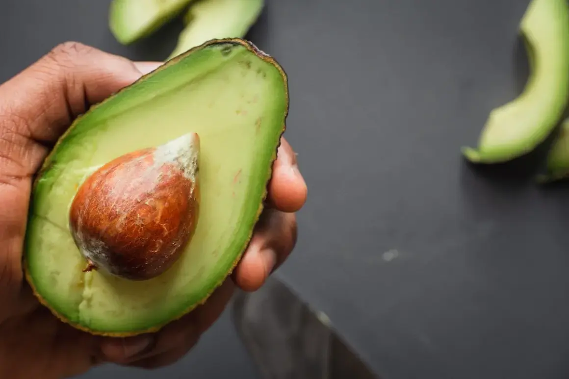 Mano che tiene mezzo avocado maturo con nocciolo. Ecco come si mangia l'avocado: fresco, cremoso, delizioso.