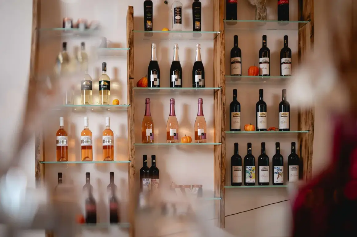 Scaffali di vetro con bottiglie di vino, tra cui spiccano bottiglie di Chiaretto del Garda dal colore rosato, accanto a zucche decorative.