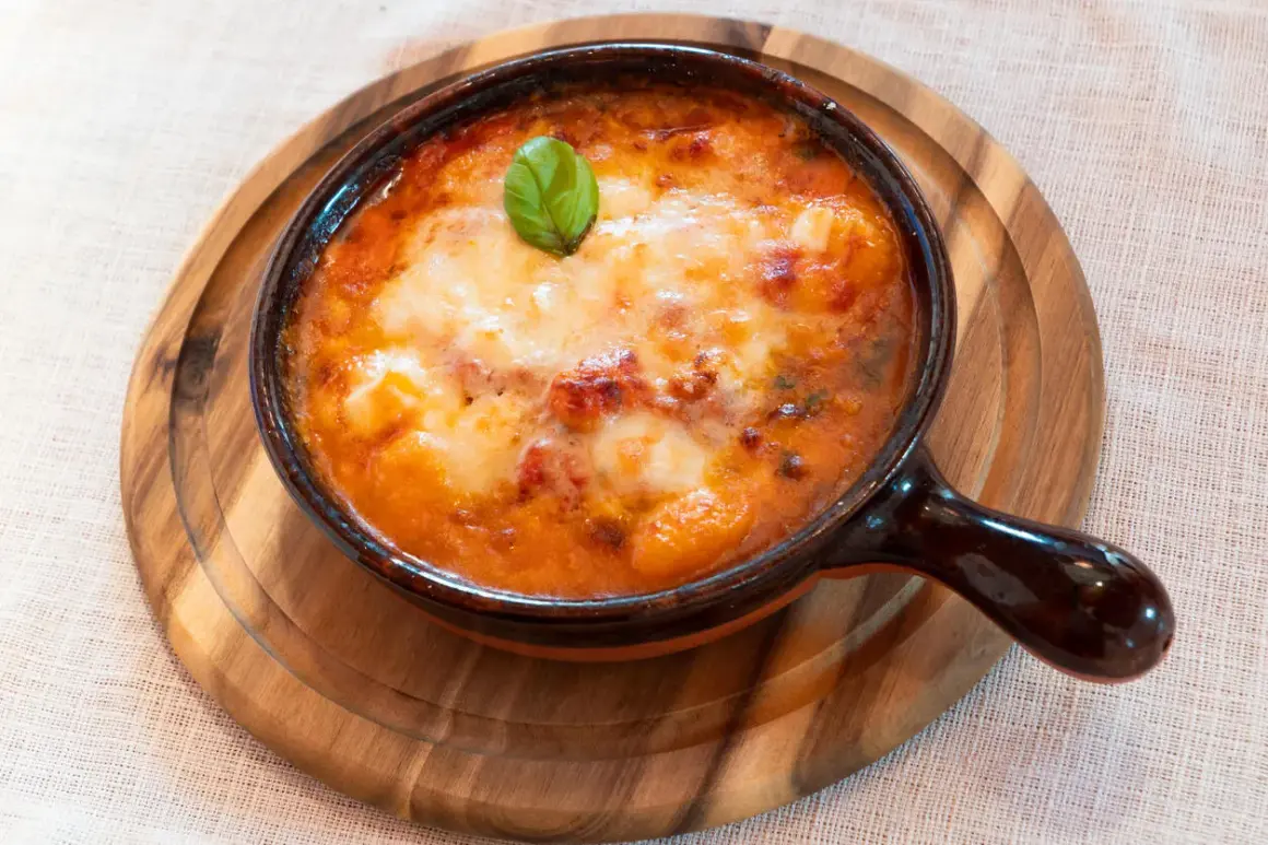 Piatto fumante di gnocchi al forno, uno dei piatti tipici della Campania, con pomodoro e mozzarella filante, guarnito con basilico.
