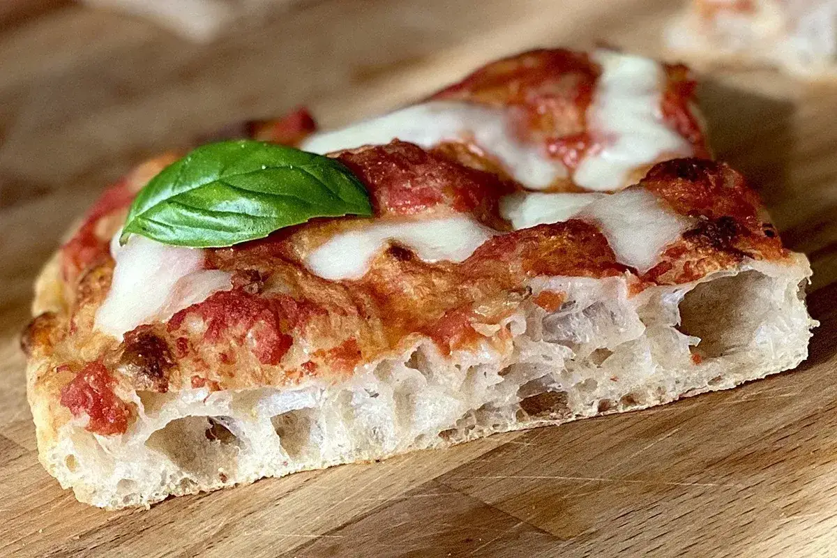 Fetta di pizza in teglia con alveolatura perfetta, pomodoro, mozzarella filante e basilico. La migliore farina per pizza in teglia fa la differenza.