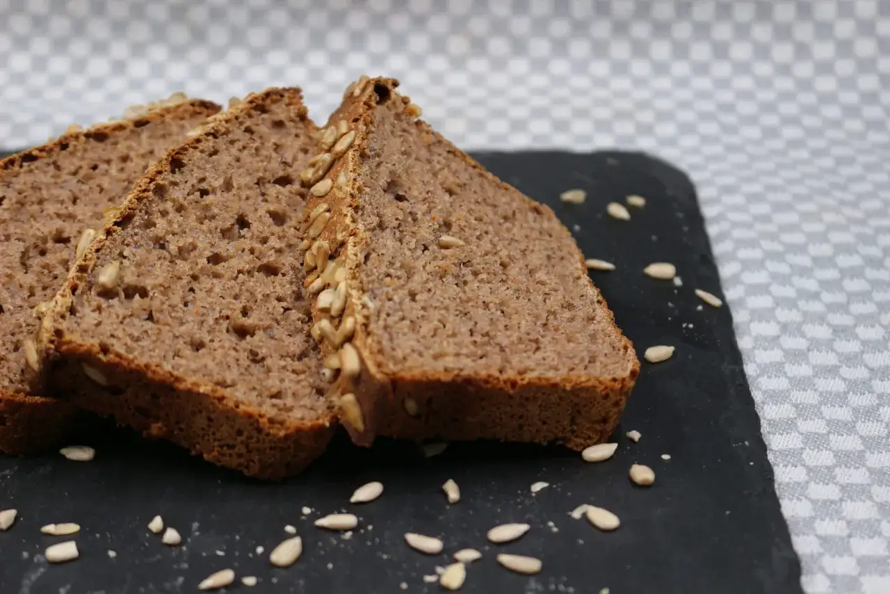 Fette di pane di grano saraceno con semi di girasole su una lavagna scura.
