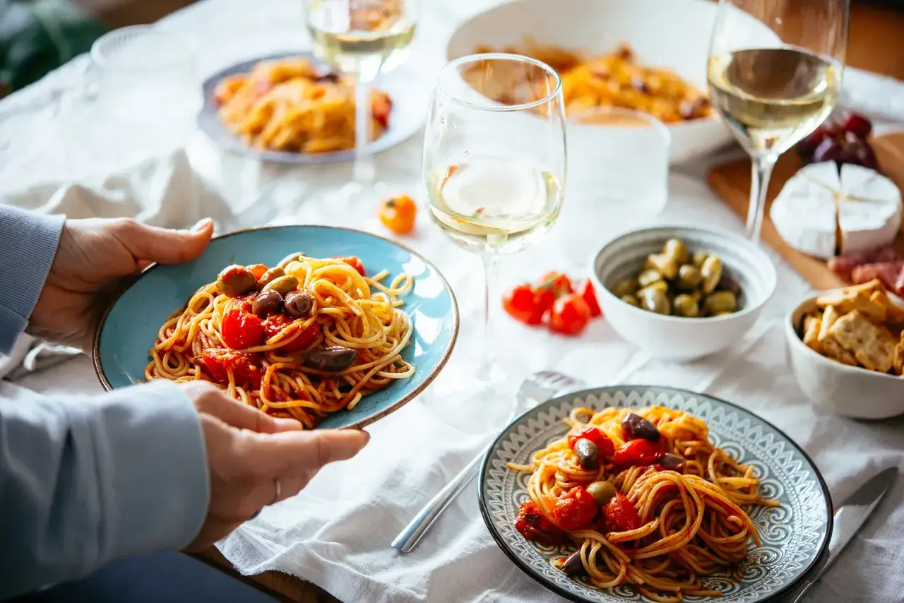 Un piatto di spaghetti con pomodorini e olive, perfetto per le tue cucina italiana ricette. Vino bianco e formaggio completano la tavola.