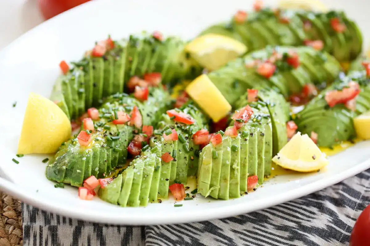 Avocado affettato a ventaglio, condito con pomodoro, erba cipollina e limone. Un modo delizioso per scoprire come si mangia l'avocado.